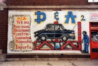 A smashed vehicle on a lift with a mechanic. D&A Auto Body Repair, Western Avenue and 47th Street-Roadside Art
