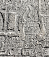 UJH 59 in figure approaching seated Mesoamerican skeleton, detail. This carver typically reversed his numbers and letters. Chicago lakefront stone carvings between Foster Avenue and Bryn Mawr. 2013.