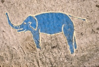 Elephant carving painted blue, with human figure underneath. Aron Packer photo. Chicago lakefront stone carvings, Montrose Harbor. 1986